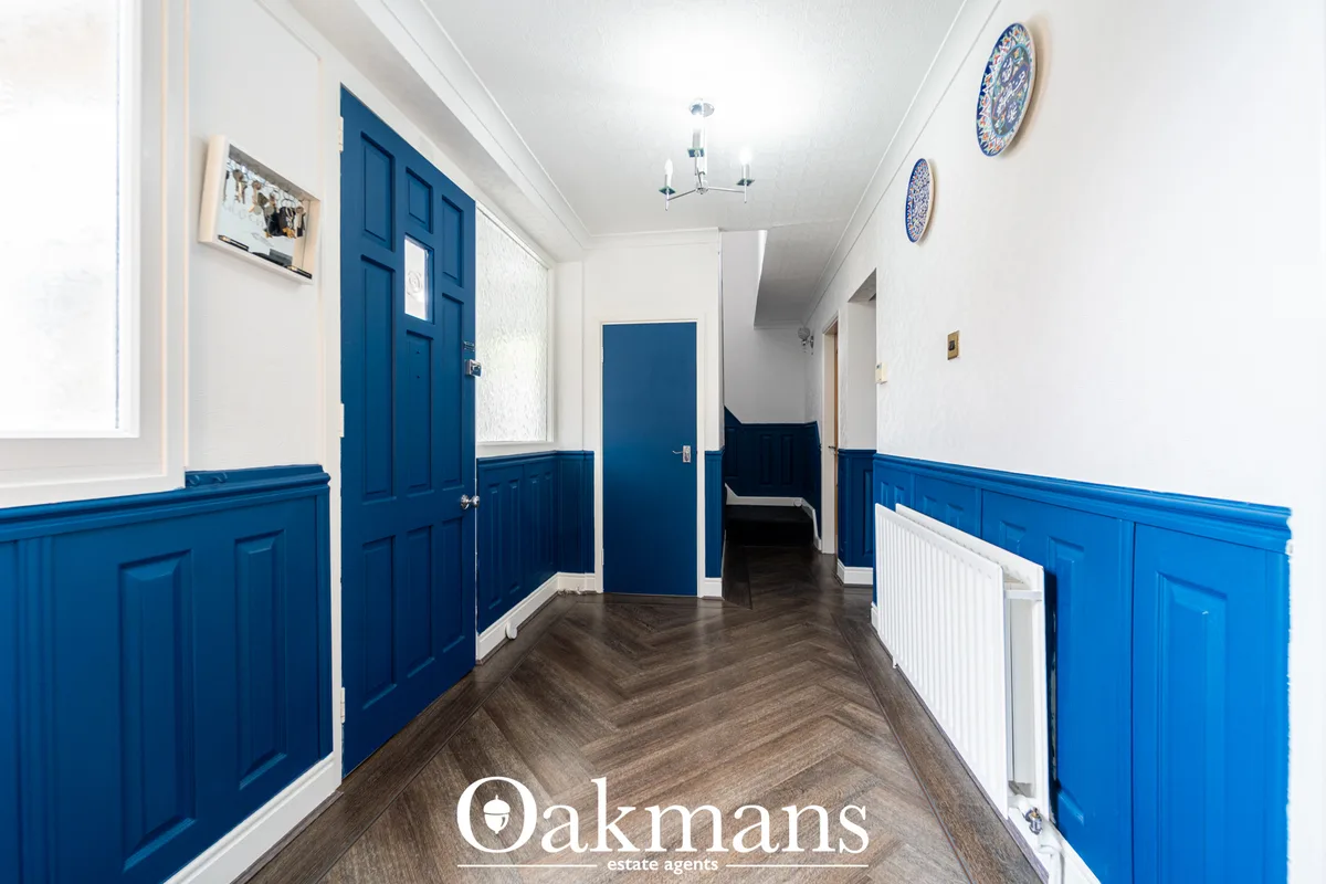 Bright hallway with striking blue panelled wainscoting, dark herringbone flooring, white walls, ceiling light and decora