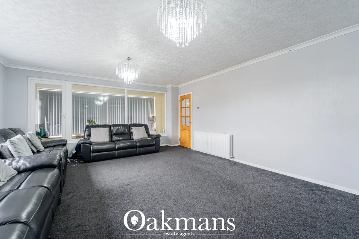 Spacious living room with grey carpet, black leather sofas, large patio doors with vertical blinds, two crystal ceiling 