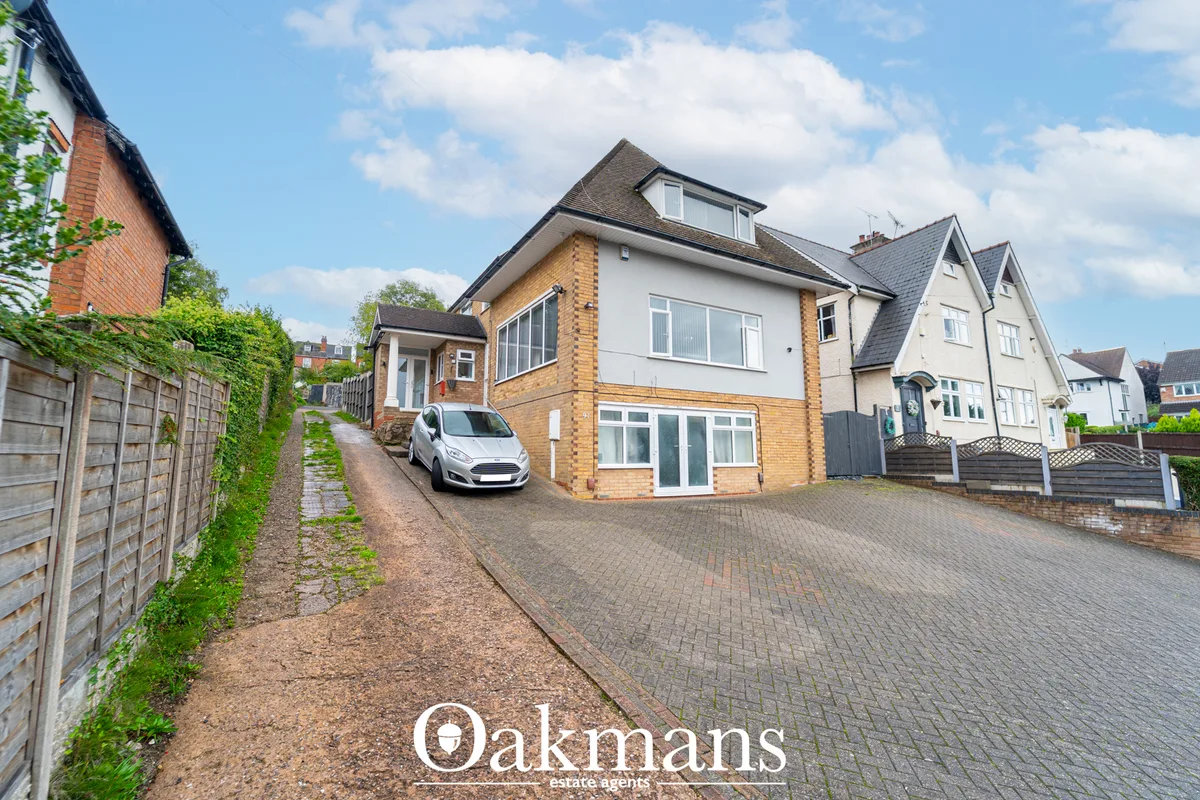 Modern two-storey detached house with brick and white render, pitched roof, driveway with parked white car, neighbouring