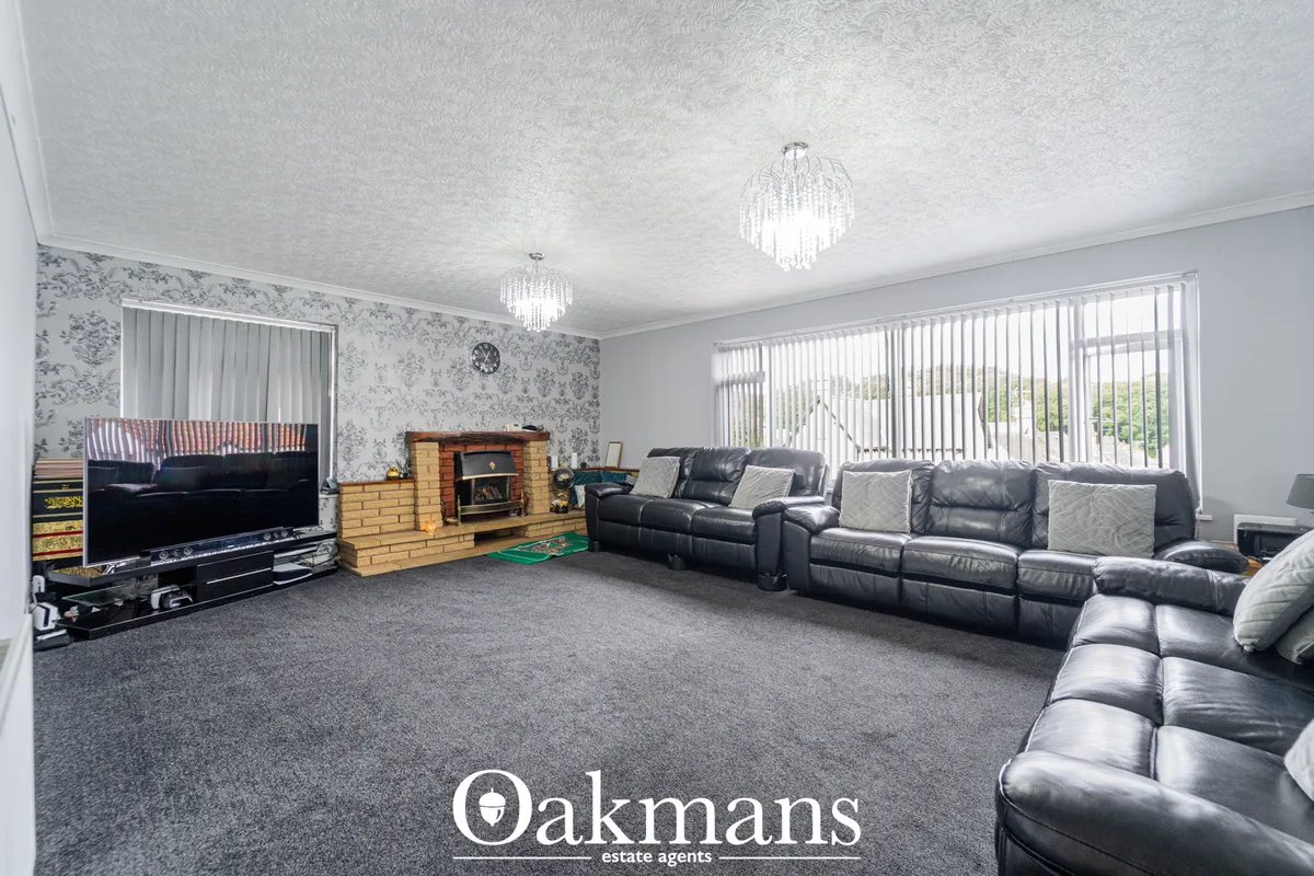 Spacious living room with dark leather sofas, brick fireplace with stove, large wall-mounted TV, patterned wallpaper and