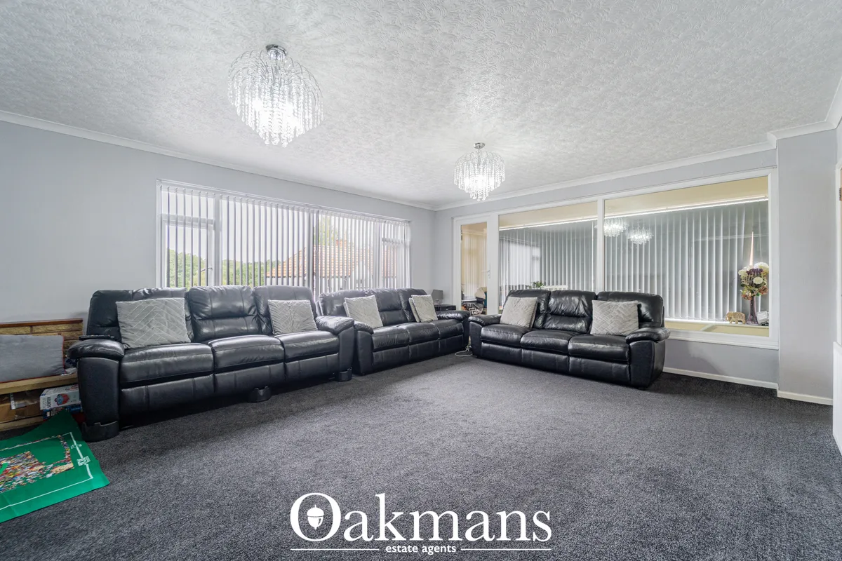 Spacious living room with two black leather reclining sofas, grey carpet, crystal ceiling lights, vertical blinds and pa