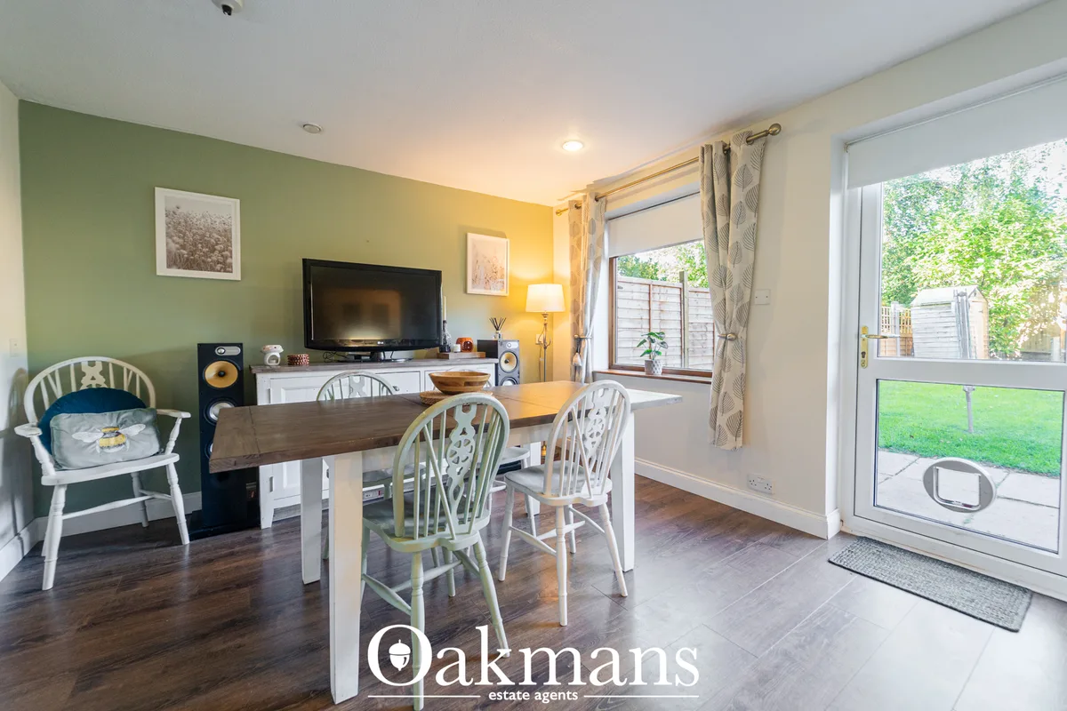 Open-plan dining and living space with wooden table, white spindle chairs, green accent wall, TV unit, and patio doors t