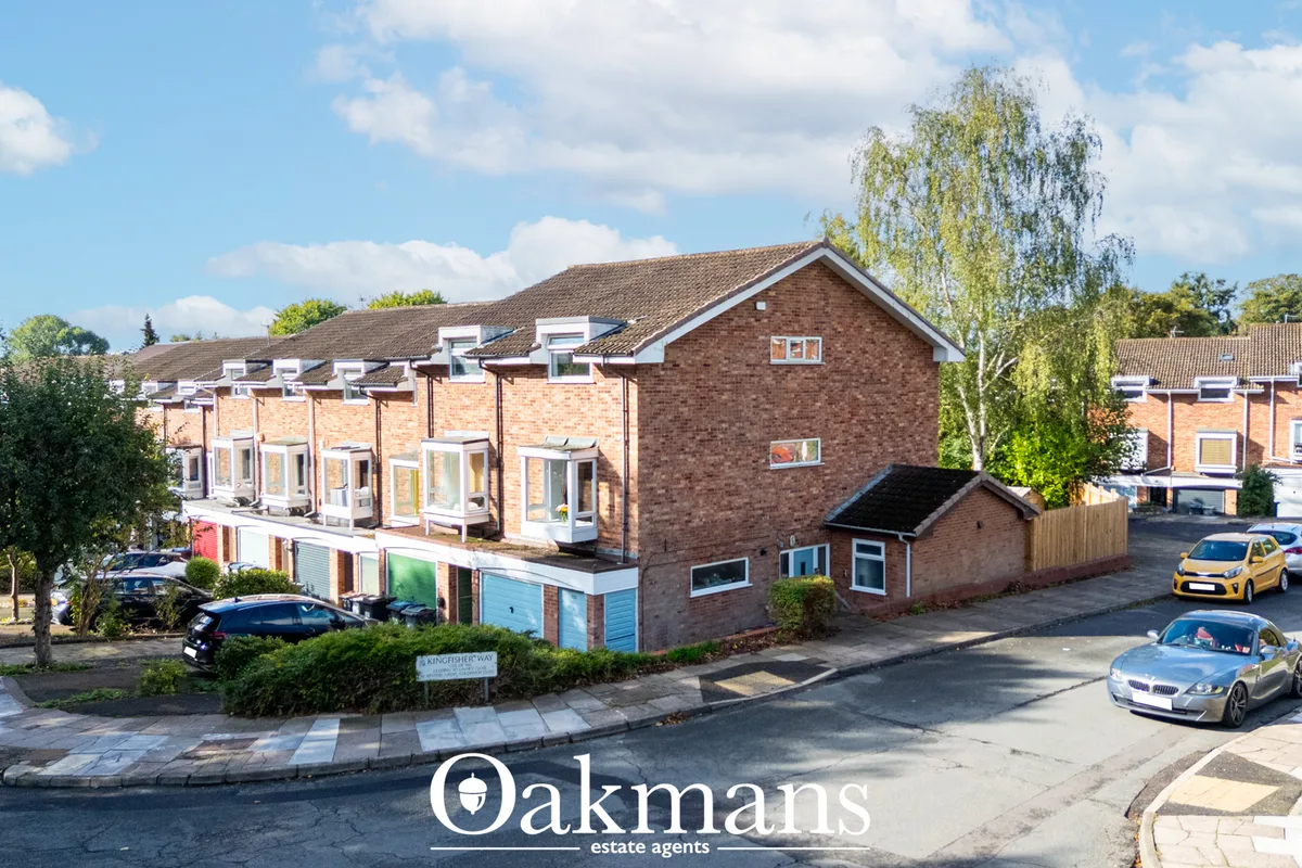 Modern brick residential building with multiple units, dormer windows, parking area with vehicles, trees and landscaping
