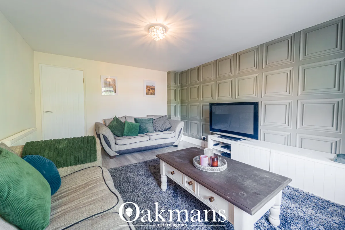 Spacious living room with cream sofa, green armchair, dark wood coffee table, flat-screen TV on white media unit, and de