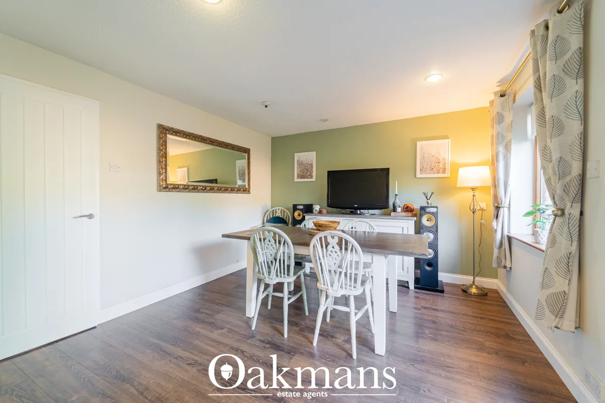 Open-plan dining area with wooden table, white Windsor chairs, green accent wall, TV unit, and decorative mirror