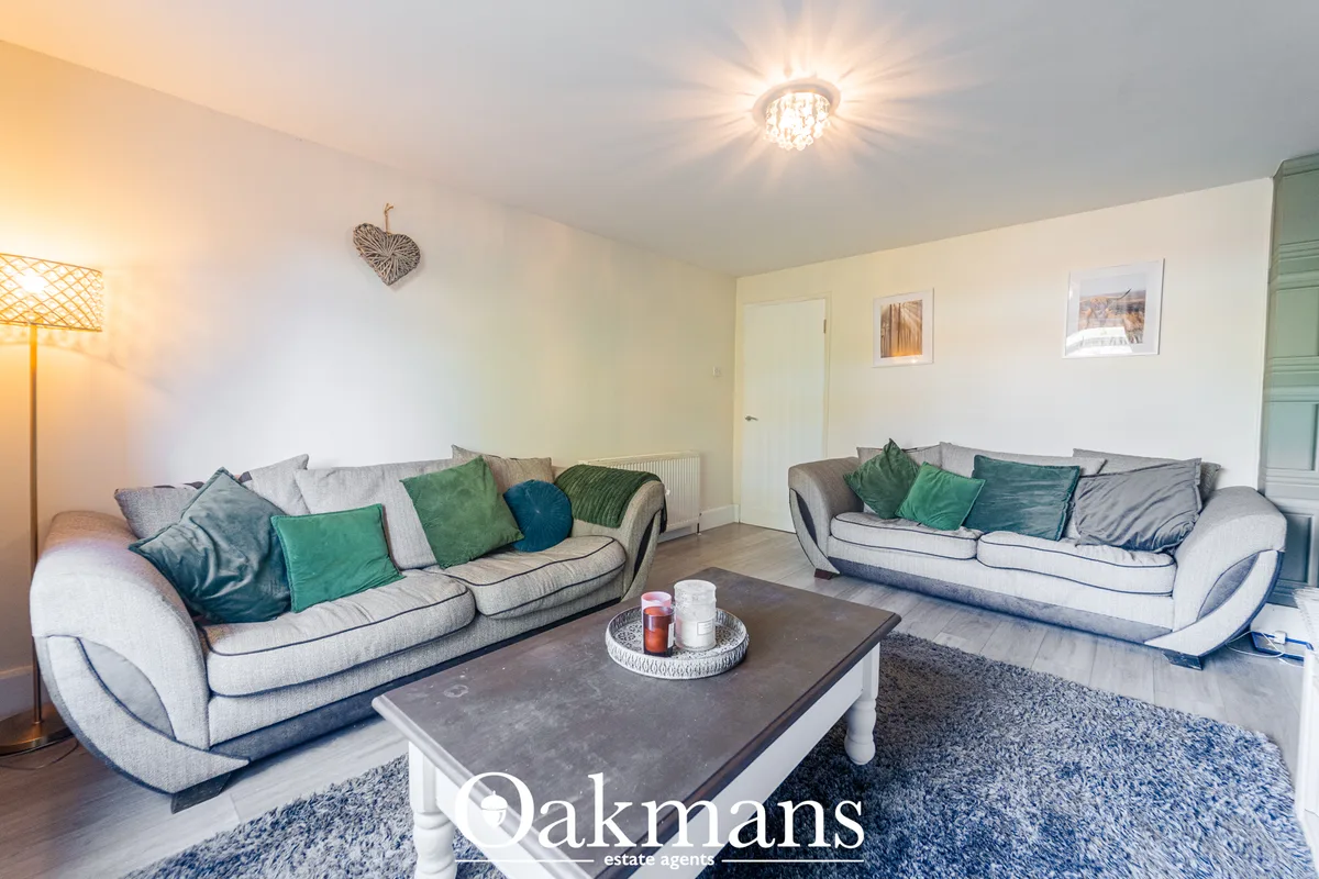 Bright living room with two light gray sofas, green and teal cushions, dark coffee table, floor lamp, and decorated with