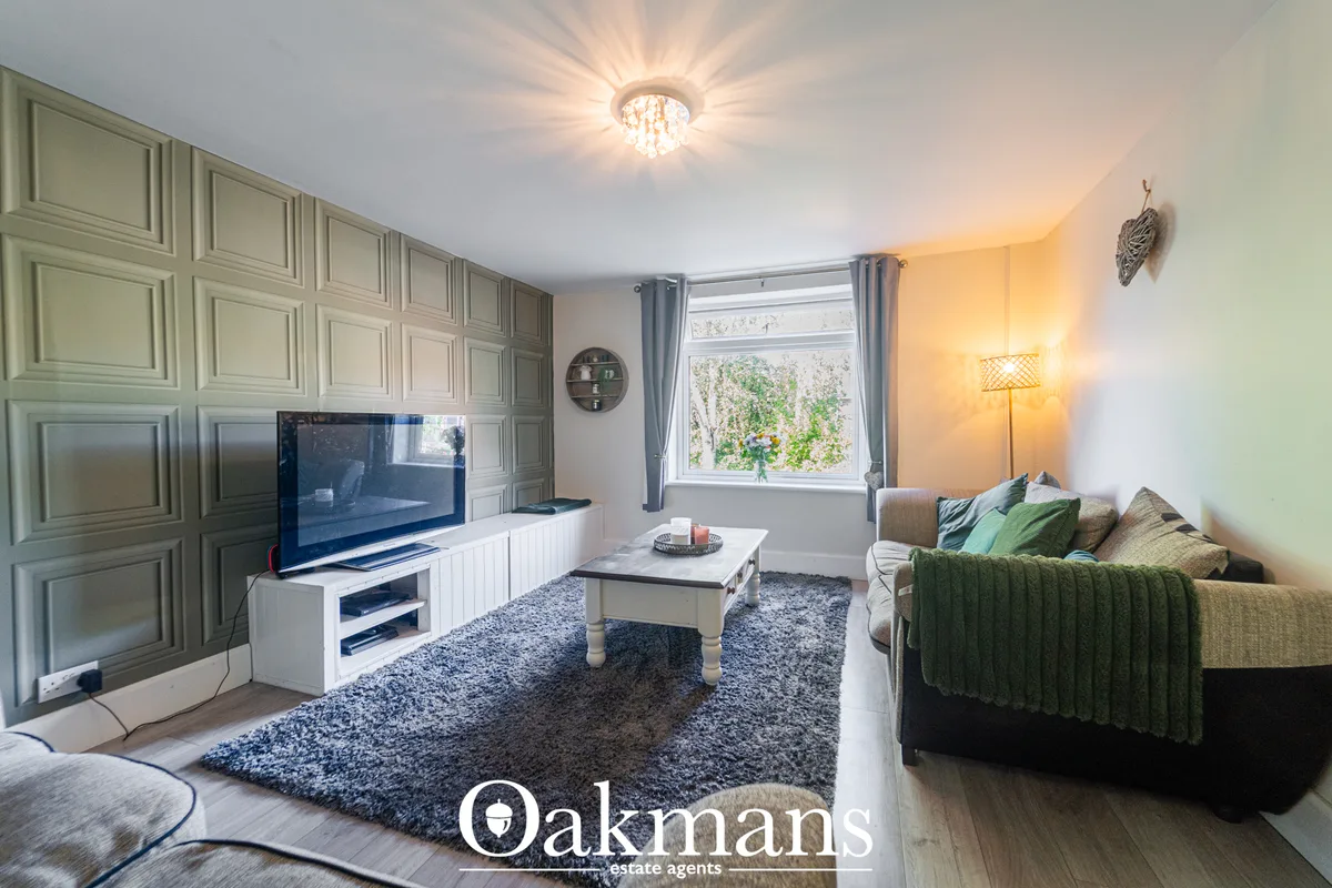 Spacious living room with grey sofa, white TV unit, coffee table, large window with garden view, grey rug and warm light