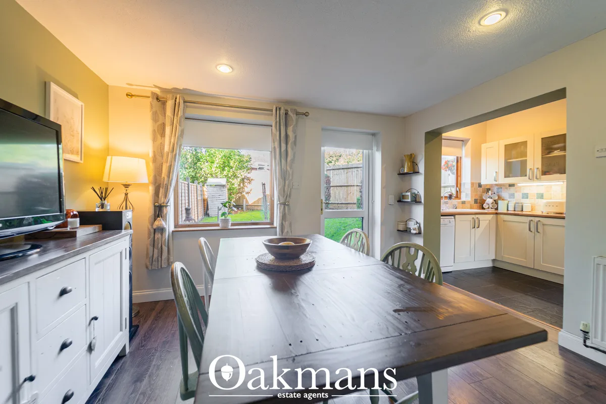 Modern open-plan kitchen with white units, dark wood dining table, four chairs, yellow accent wall, garden views through