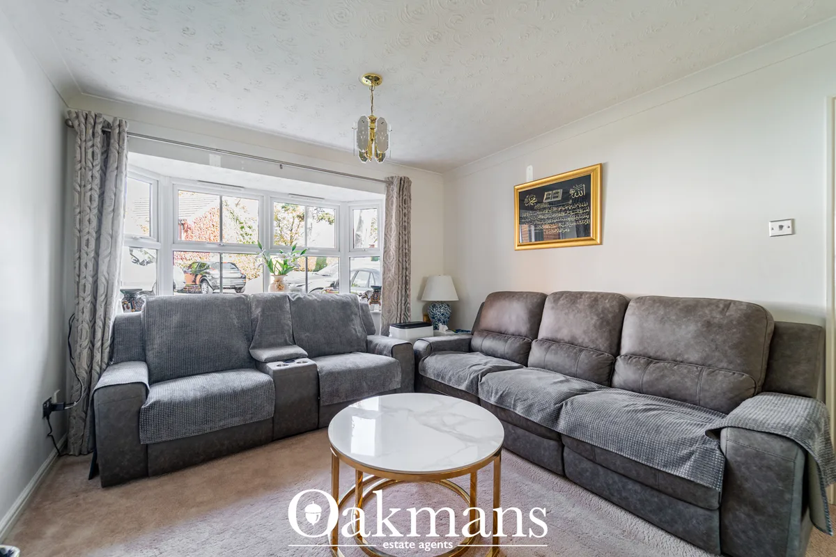 Spacious living room with two grey upholstered sofas, round marble coffee table, large bay window with grey curtains, an