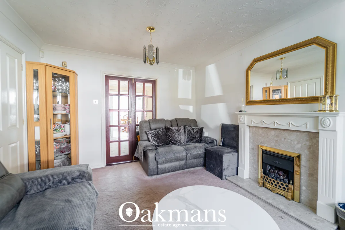 Spacious living room with grey sofas, fireplace with white mantelpiece and gold-framed mirror, wooden display cabinet, a