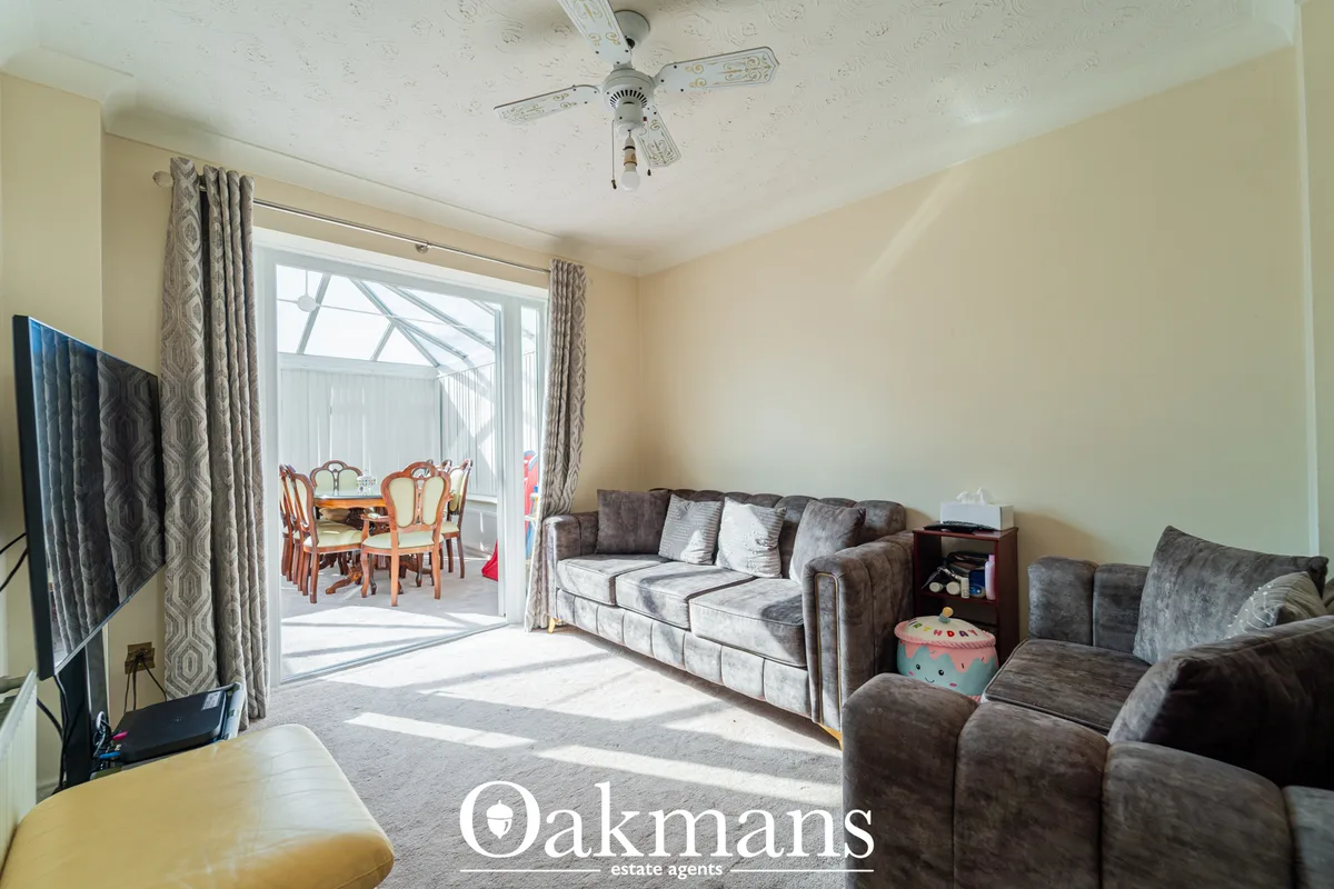 Spacious living room with grey upholstered sofa, armchair, ceiling fan, patio doors opening to conservatory with dining 