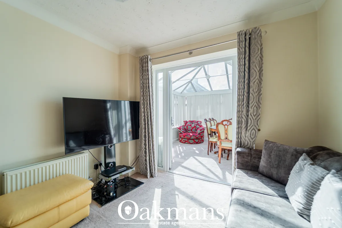 Bright living room with cream walls, grey patterned curtains, flat-screen TV on stand, grey upholstered sofa, yellow arm
