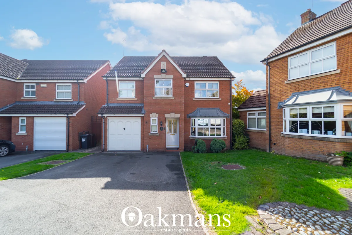 Red brick detached house with white garage doors, bay windows, driveway and manicured front garden under blue sky