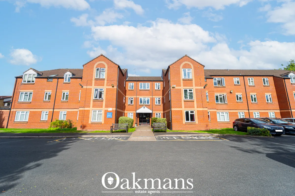 Front elevation of modern red-brick apartment building with symmetrical gabled roofs, white window frames, central entra