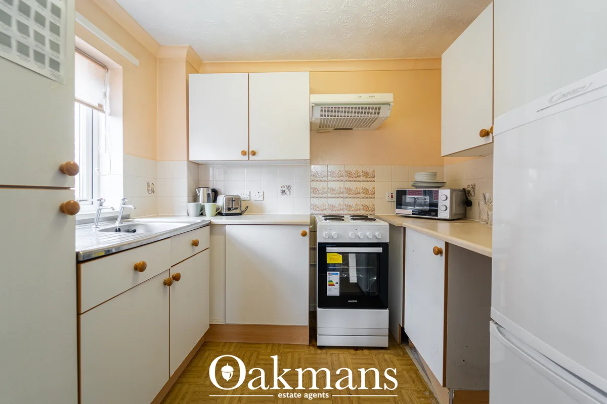 Compact fitted kitchen with cream and white units, wooden handles, peach walls, gas cooker, and window overlooking stree