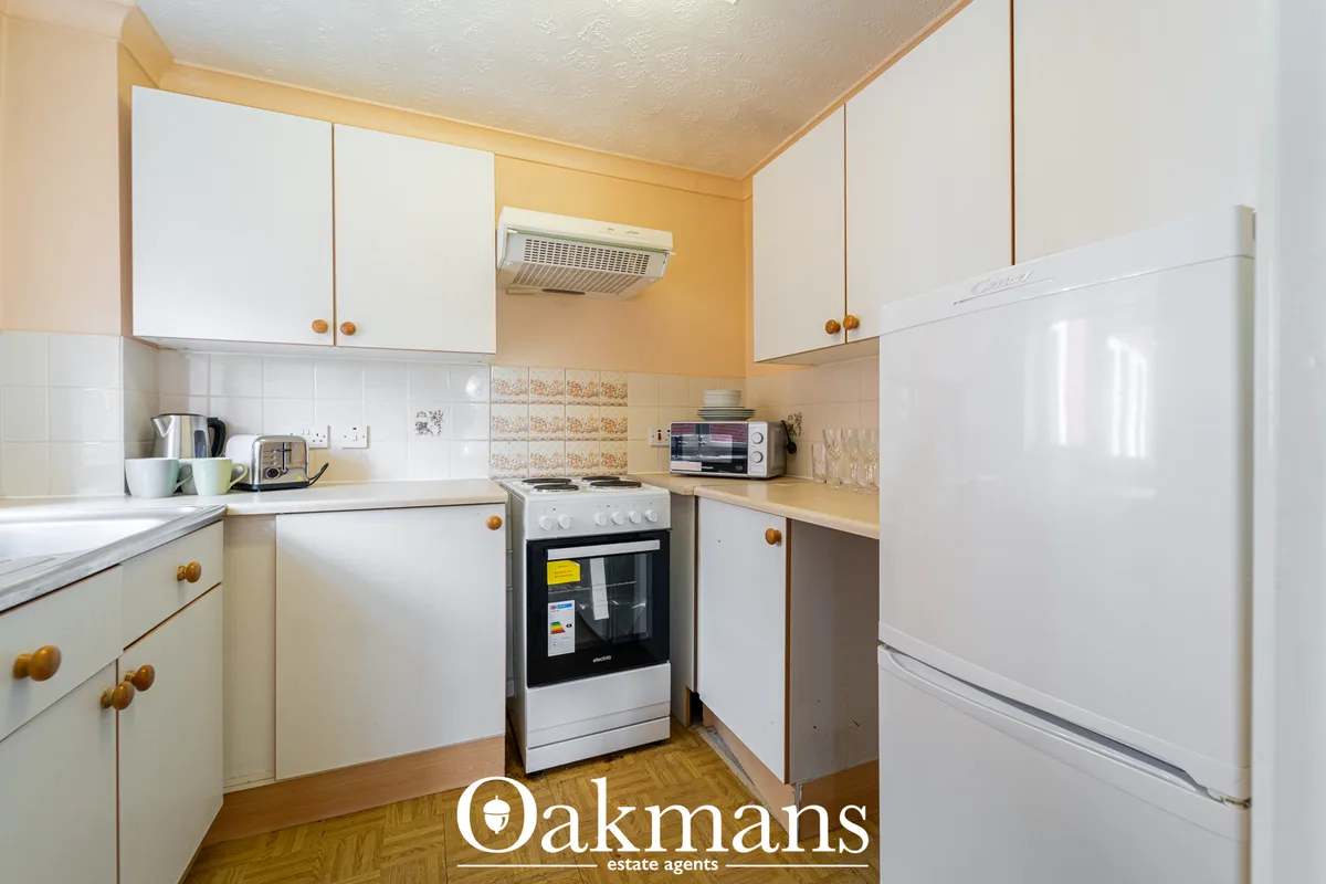 Compact fitted kitchen with white cabinetry, wooden worktops, cream range cooker, white refrigerator and modern wall uni