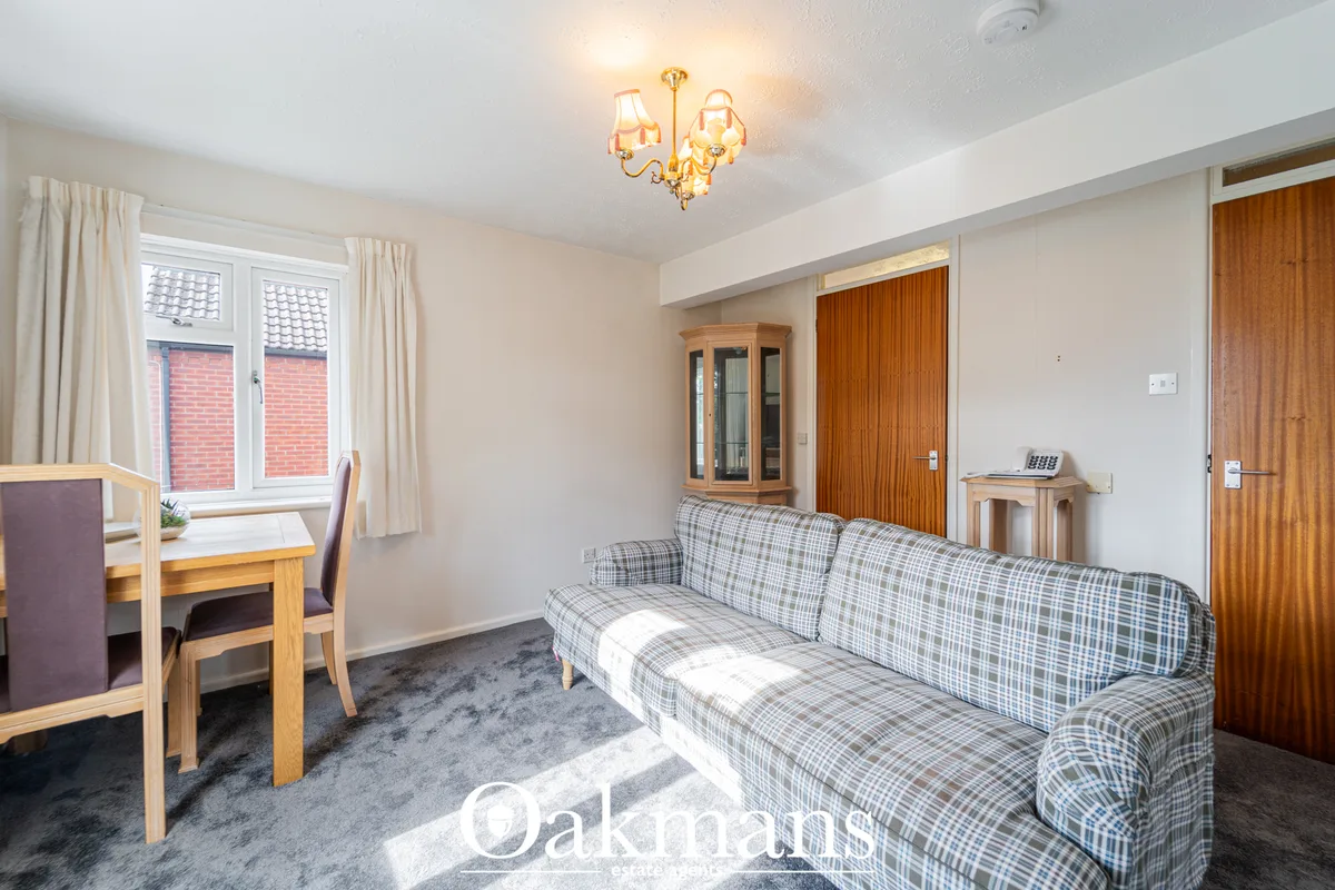 Spacious living room with checkered sofa, wooden desk, cream curtains, chandelier, and doors to other rooms