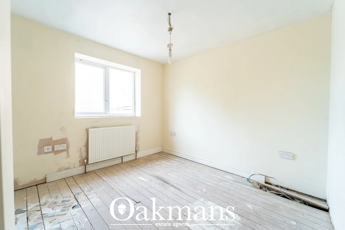 Empty bedroom with cream walls, radiator, window, wooden floorboards and light pendant fixture during renovation