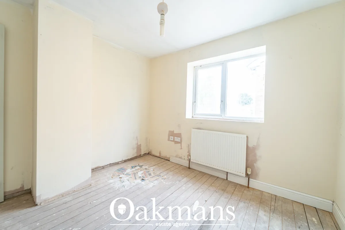 Empty bedroom with cream walls, wooden floorboards, white radiator, pendant ceiling light and double-glazed window