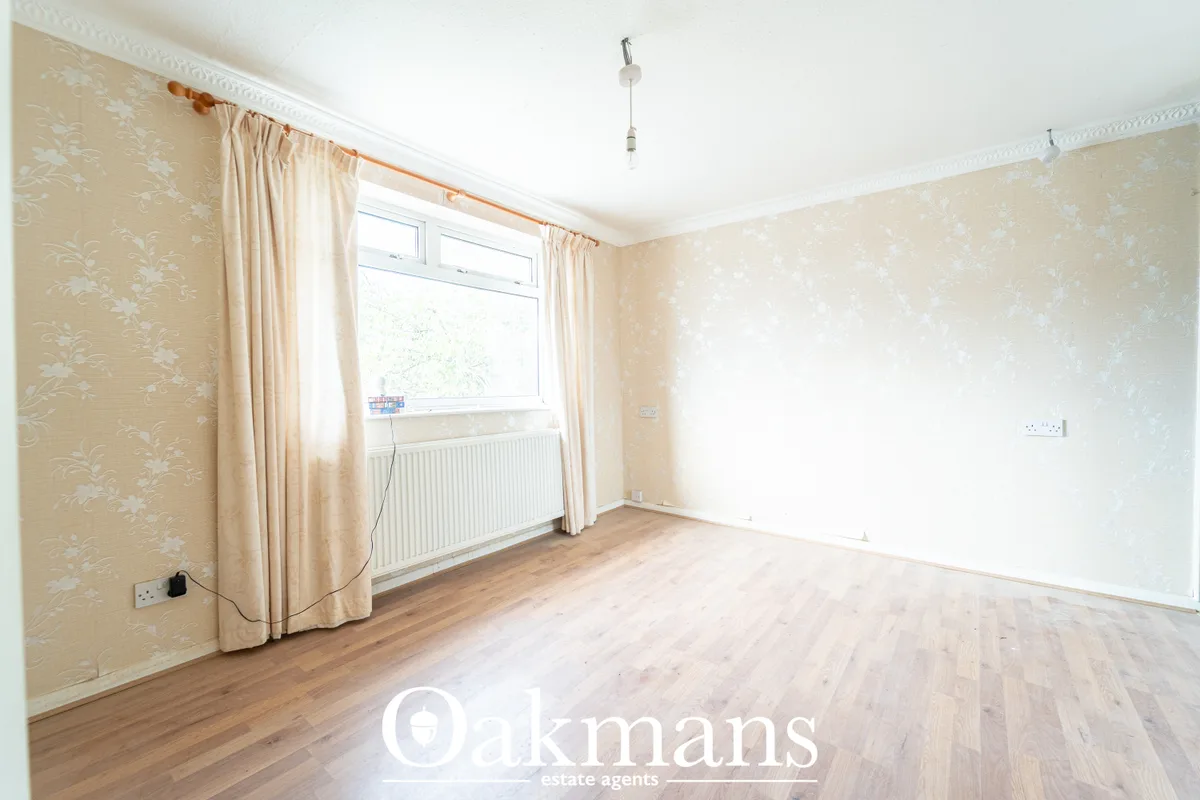 Spacious bedroom with beige patterned wallpaper, wooden flooring, large window with cream curtains, radiator, and pendan