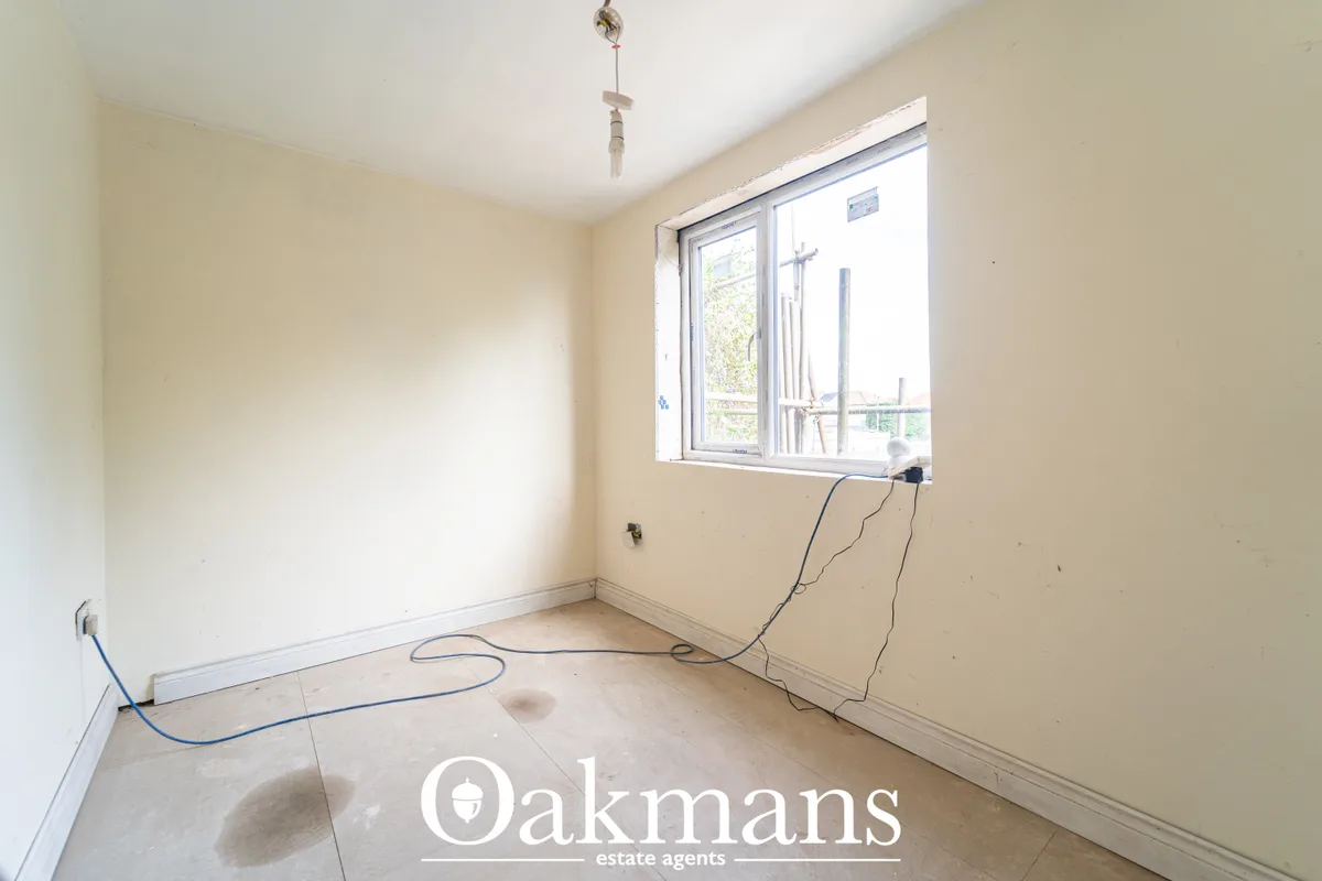 Empty bedroom with cream walls, large window with grey frame, electrical cables on floor, white skirting boards