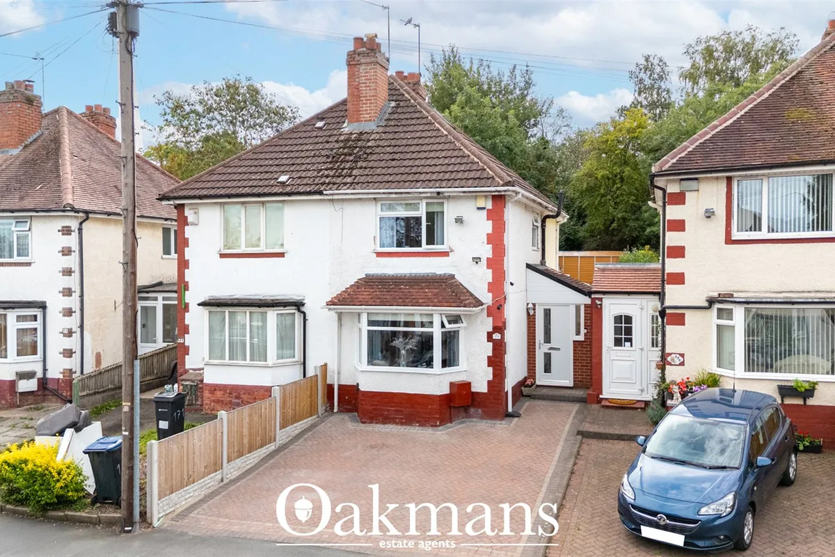 Suburban semi-detached properties with white and red brick facades, tiled roofs, parked car, wooden fencing and establis