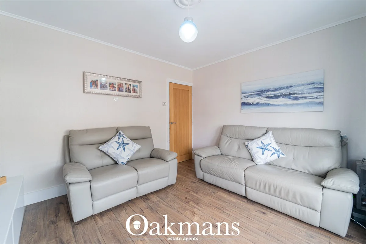 Spacious living room with two beige leather sofas, starfish cushions, wooden door, framed photos, coastal artwork, wood 