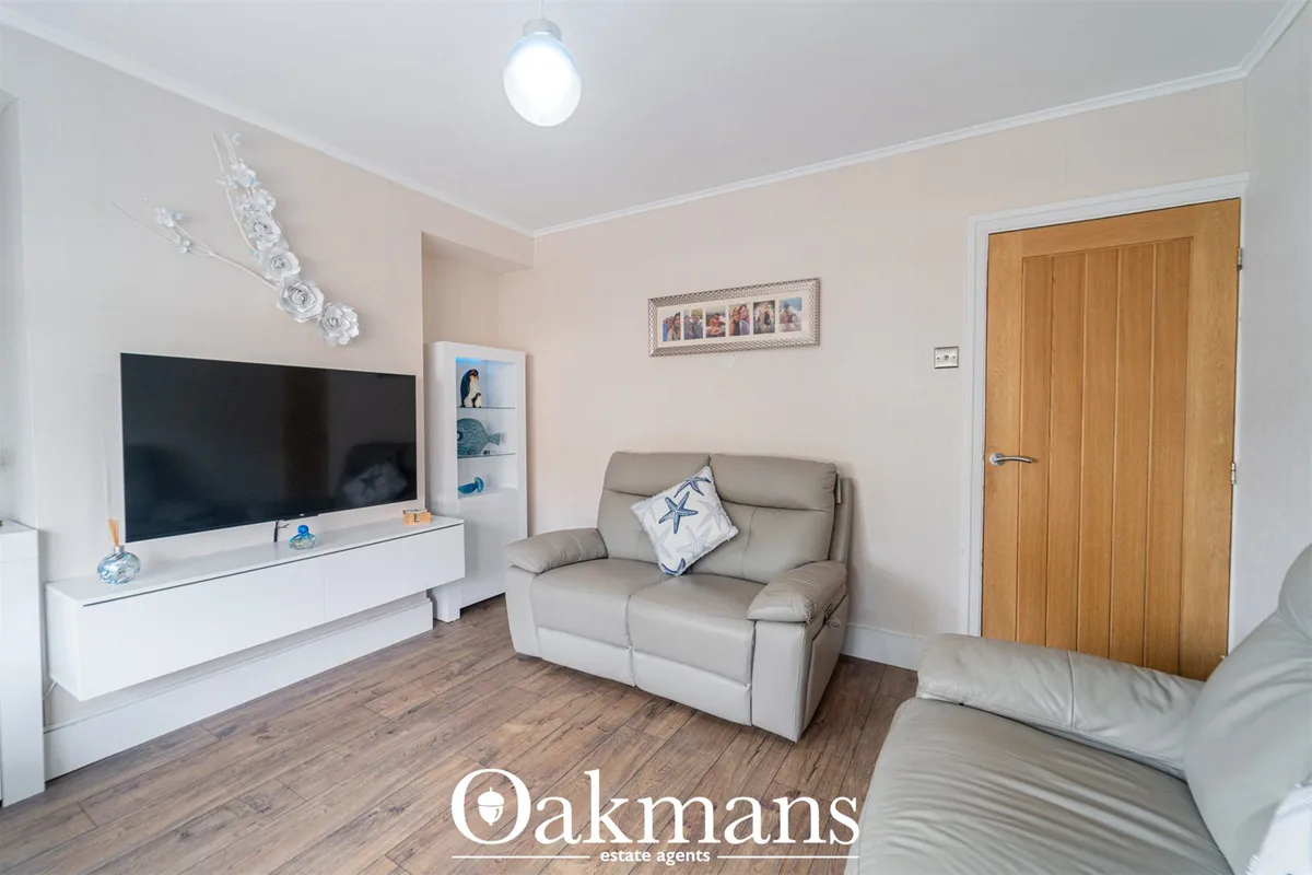 Bright living room with beige leather armchair, flat-screen TV on white unit, wooden door, pale pink walls and wood-effe