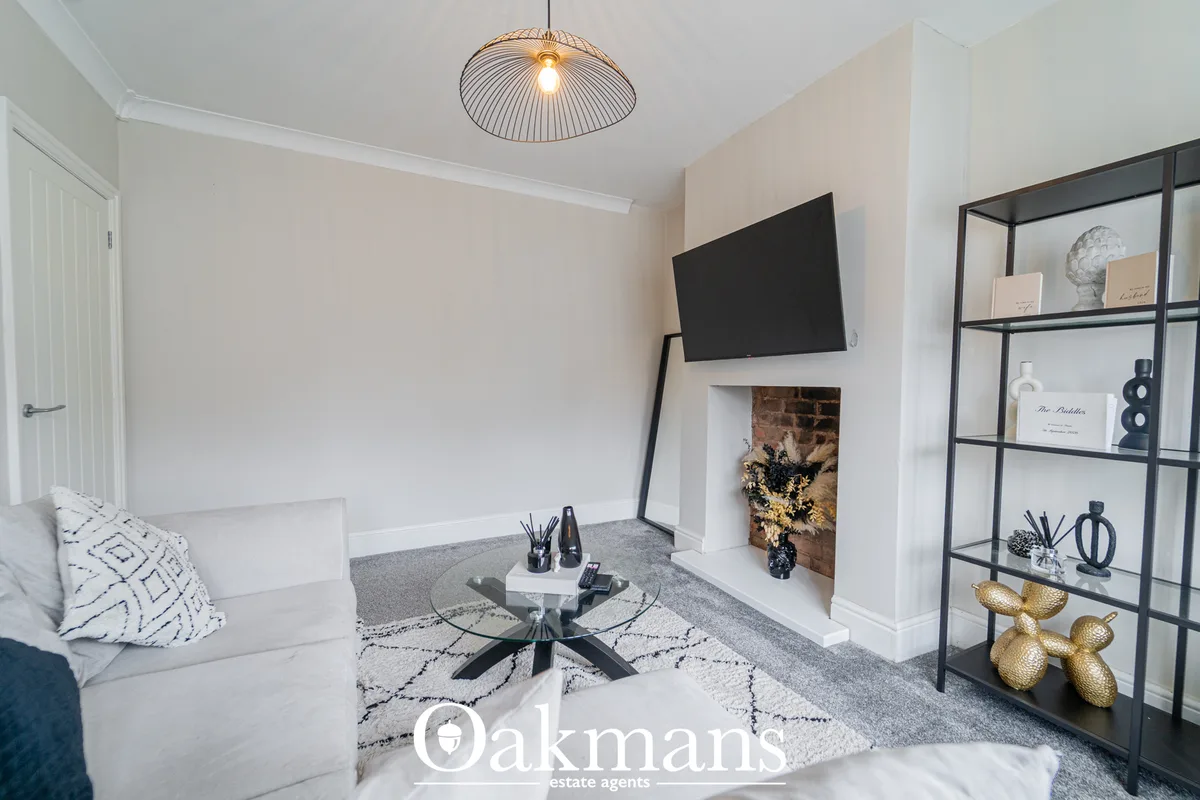 Modern living room with white sofa, glass coffee table, wall-mounted TV above fireplace, black metal shelving unit with 