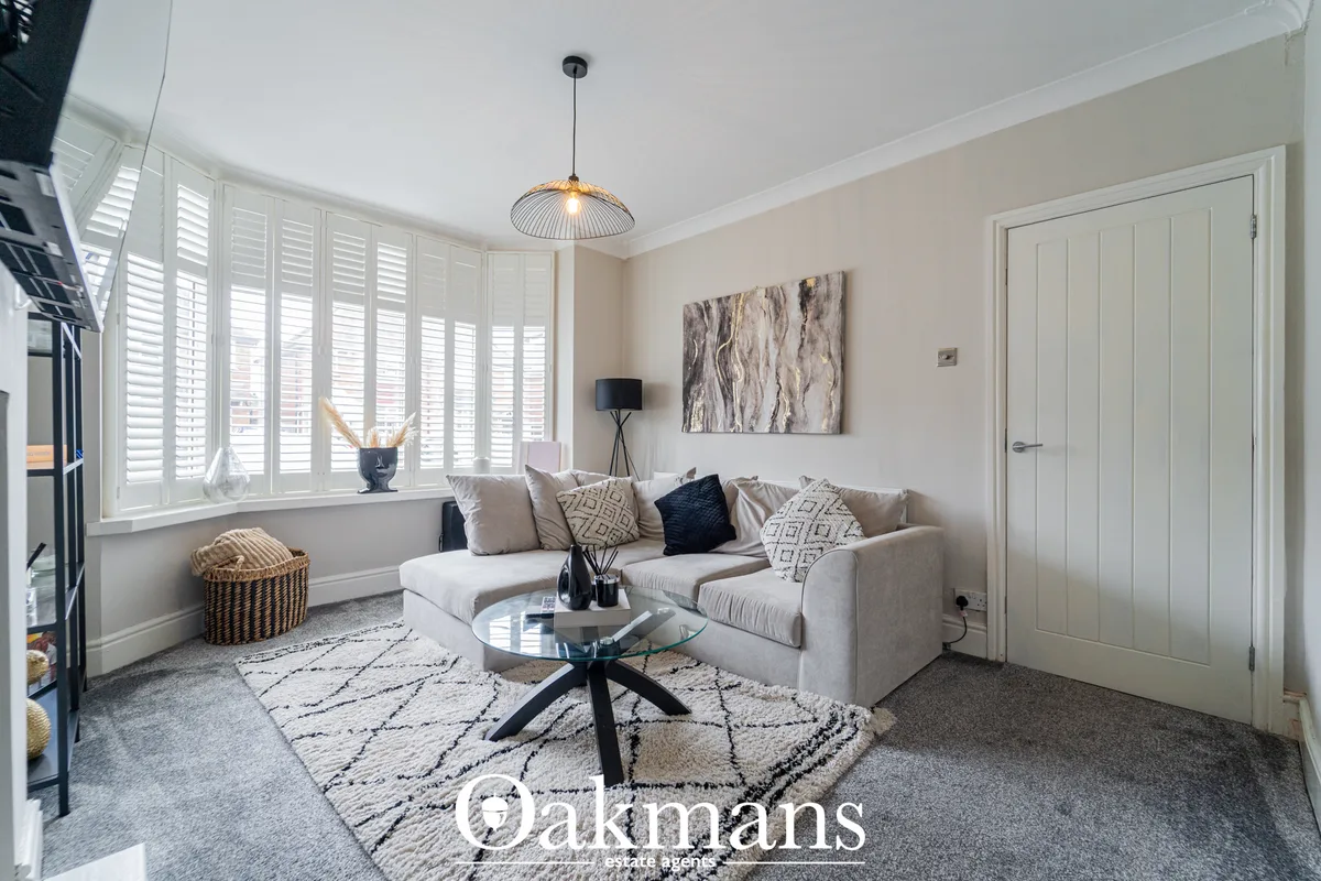 Bright living room with cream sofa, patterned cushions, glass coffee table, pendant lighting, bay window with shutters a