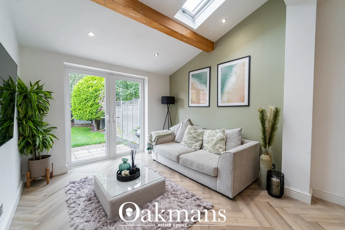 Bright conservatory with cream sofa, glass coffee table, sage green accent wall, exposed wooden beam, French doors to ga