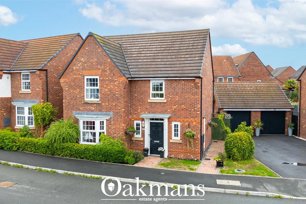 Red brick detached house with pitched roof, black front door, white bay window, hedged front garden and double garage to