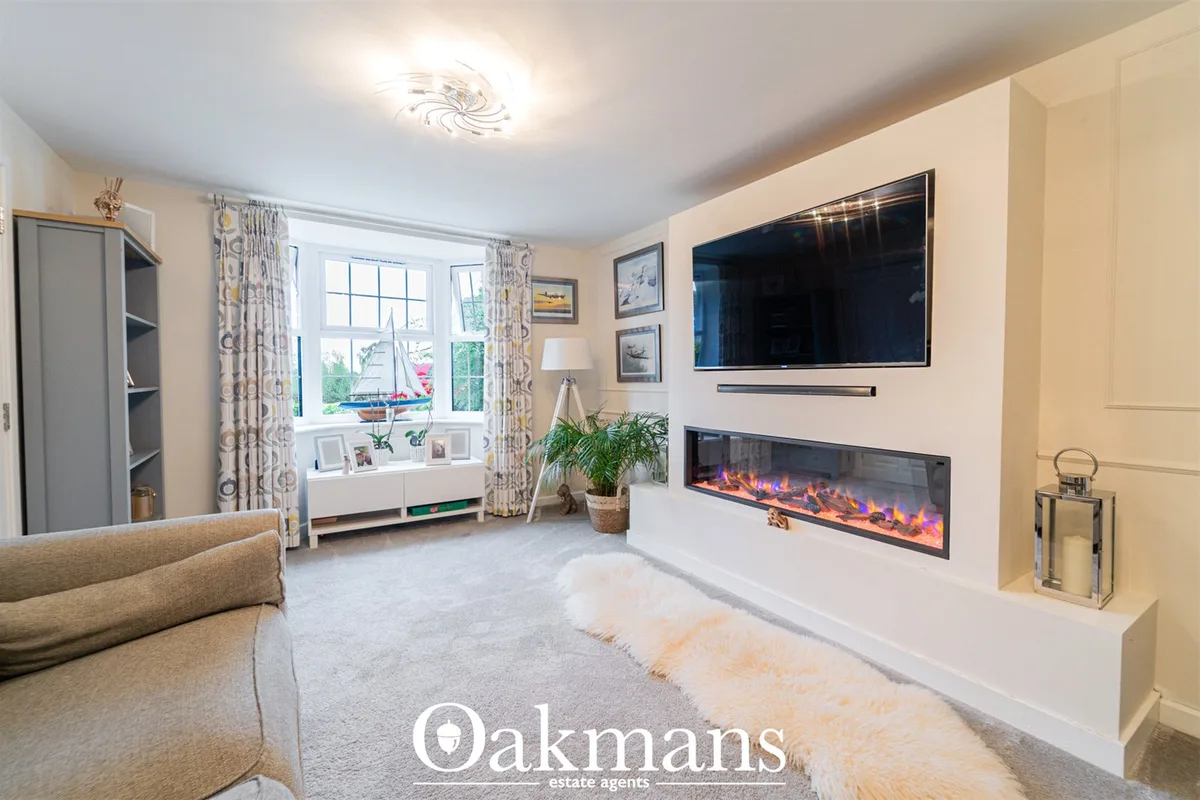 Spacious living room with cream walls, wall-mounted TV above electric fireplace, beige sofa, large bay window with decor