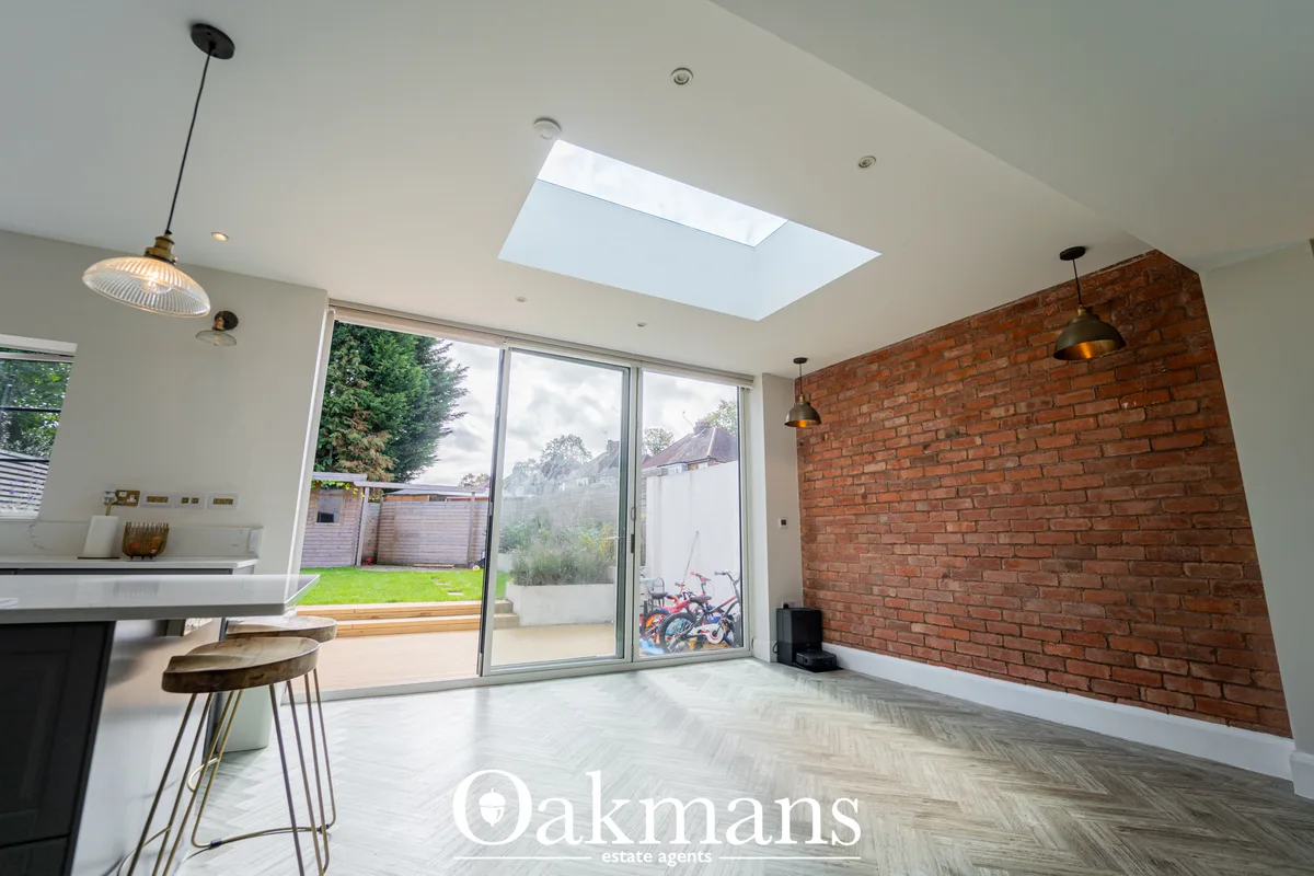 Modern open-plan living space with exposed brick feature wall, skylights, pendant lighting, herringbone flooring and lar