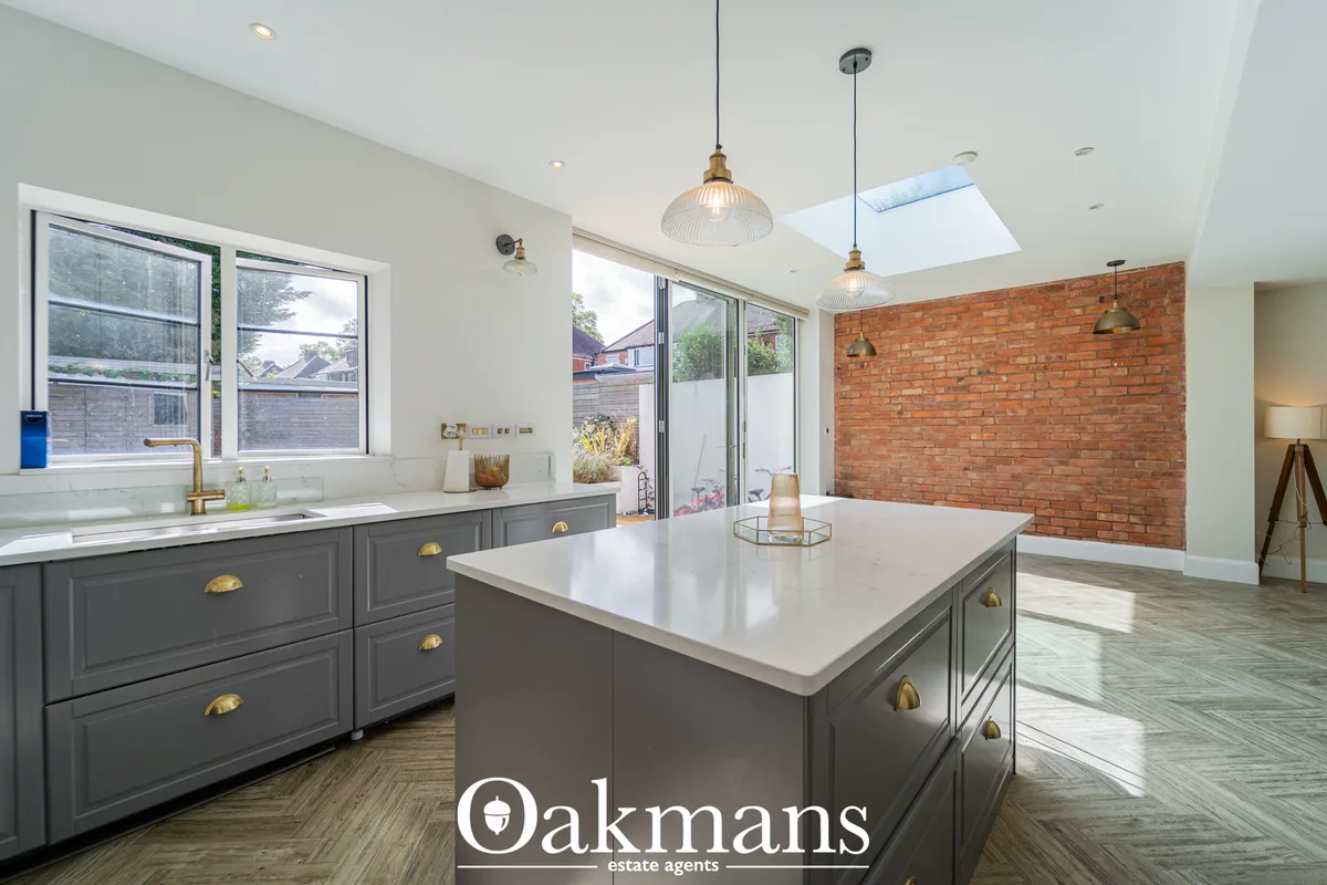 Modern open-plan kitchen with grey cabinetry, white worktops, brass fittings, pendant lighting, exposed brick accent wal