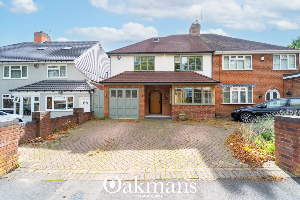 Red brick semi-detached house with double garage, driveway, and manicured front garden on residential street