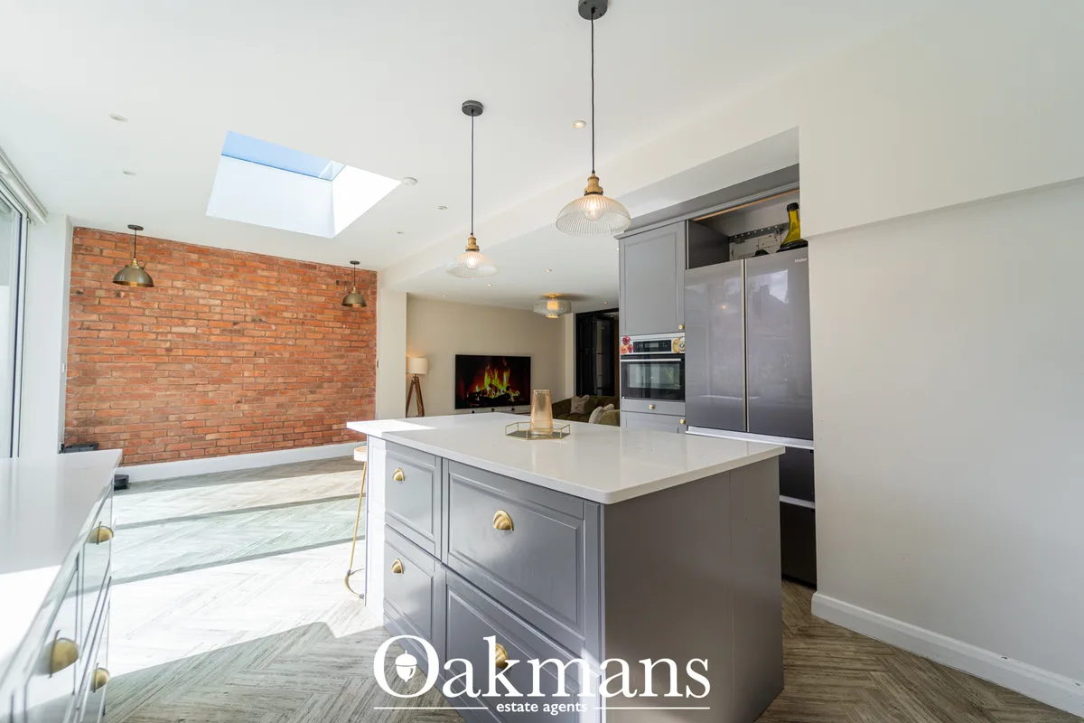 Modern open-plan kitchen with grey cabinetry, white worktops, pendant lights, exposed brick wall, skylight and integrate