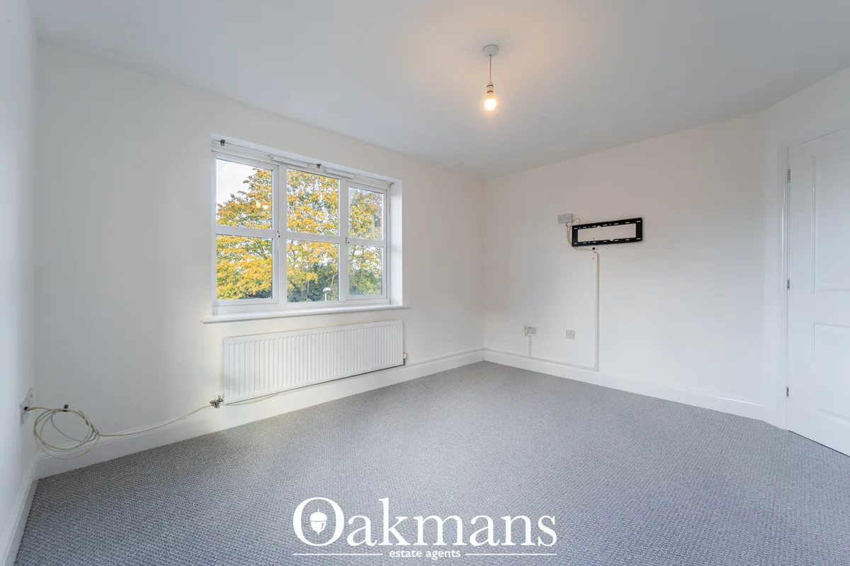 Bright bedroom with large triple-glazed window overlooking autumn trees, white radiator, grey carpet, and wall-mounted T