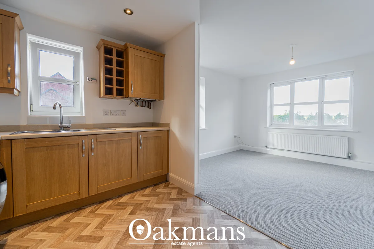 Modern fitted kitchen with wooden cabinetry, herringbone wood flooring, sink with chrome tap, and open-plan view to carp