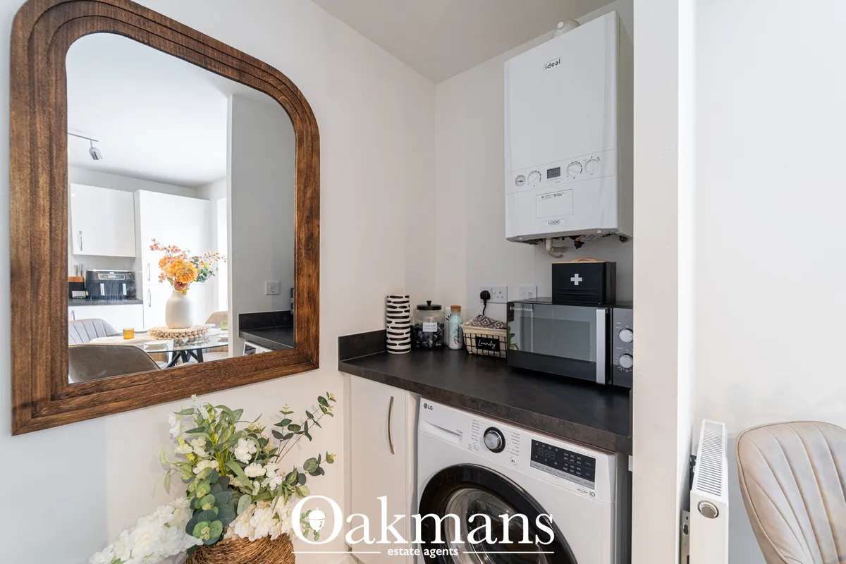 Utility room with white LG washing machine, black worktop, white wall-mounted boiler, microwave, decorative mirror and p