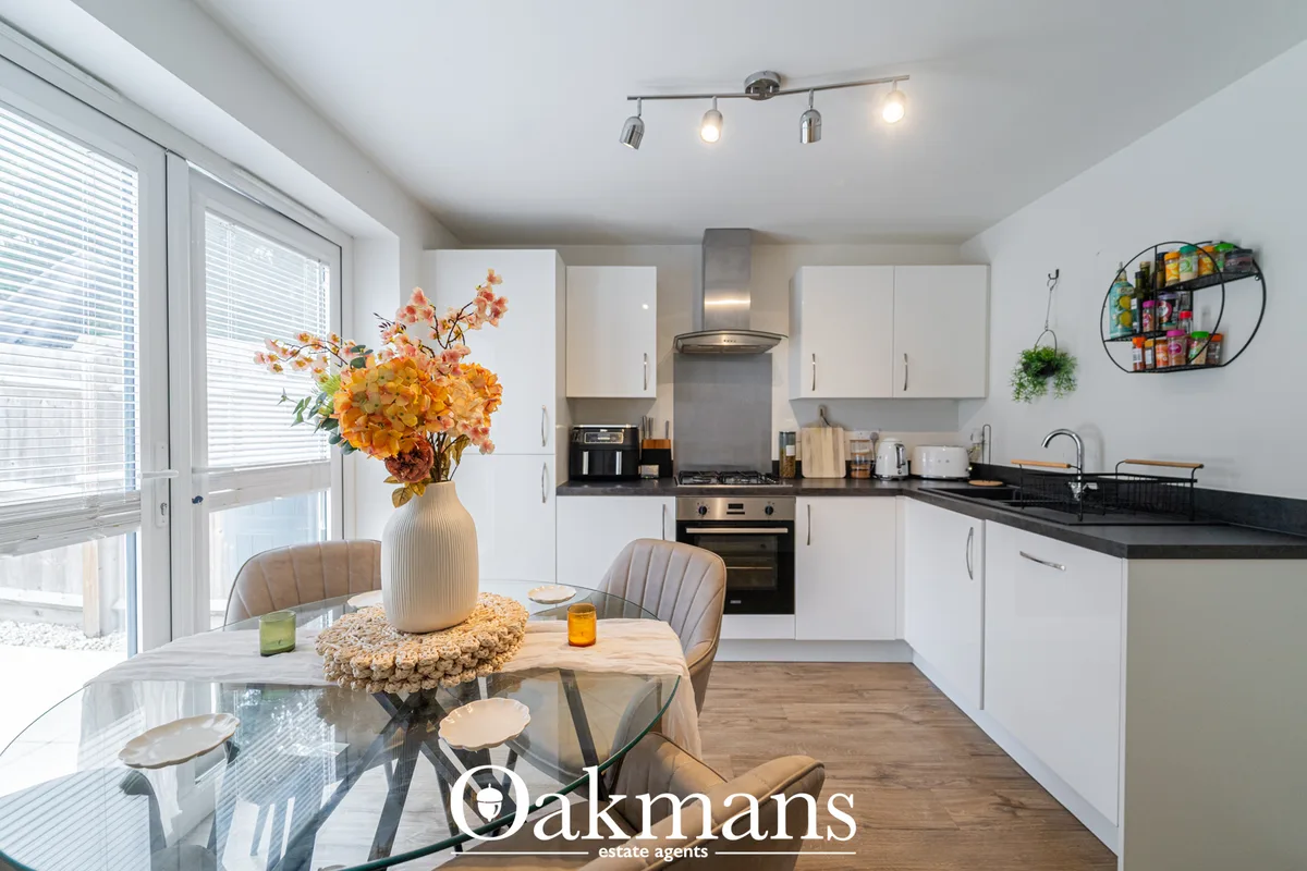 Modern fitted kitchen with white cabinetry, black granite worktops, integrated appliances, and dining area with table an