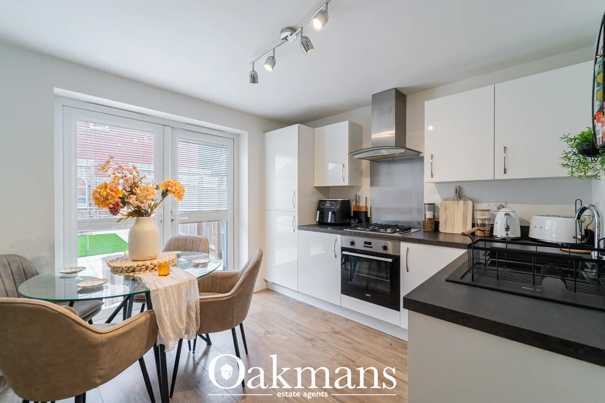 Modern fitted kitchen with white gloss units, black granite worktops, stainless steel cooker hood and hob, with dining a