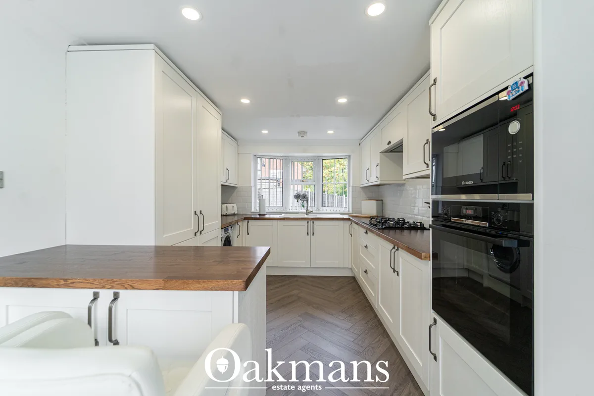 Modern fitted kitchen with cream shaker units, wooden worktops, built-in black Bosch appliances, gas hob, breakfast bar 