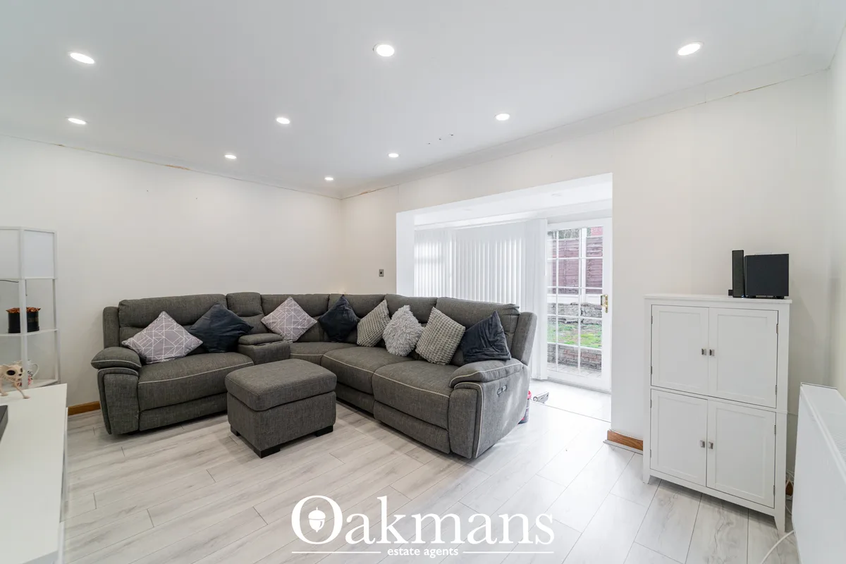 Modern living room with grey corner sofa, patterned cushions, footstool, white storage cabinets, TV, recessed ceiling li