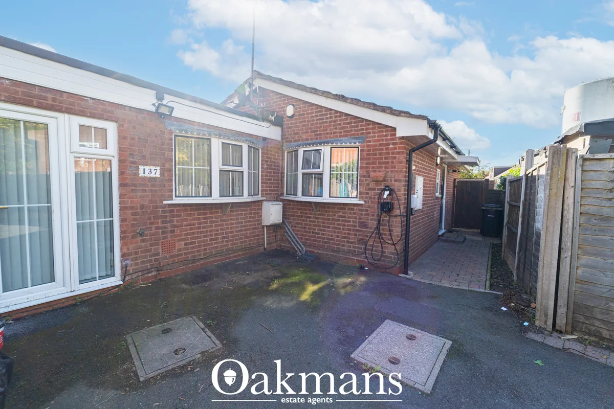 Rear courtyard of brick bungalow with paved driveway, two inspection covers, wooden fencing, water tank and electric cha