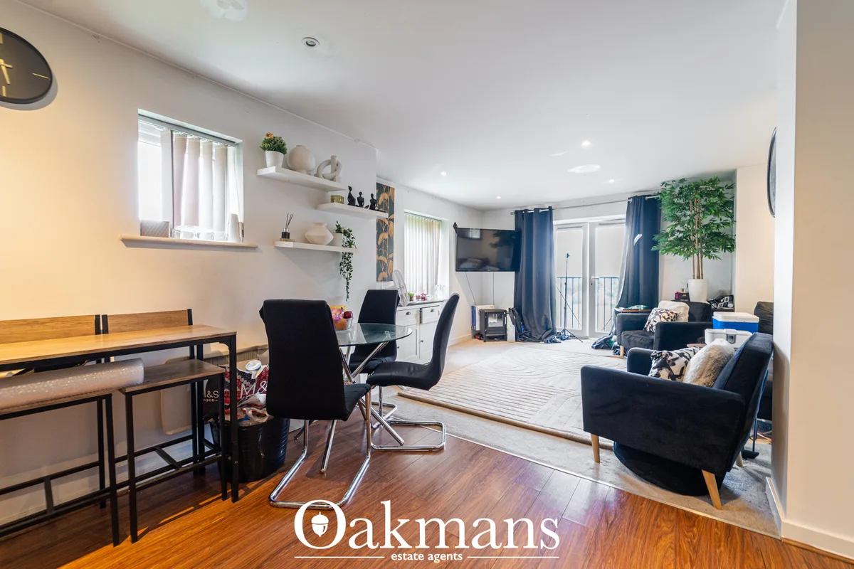 Open-plan living room with dark blue armchair, glass dining table, wooden flooring, white walls, wall-mounted TV and blu