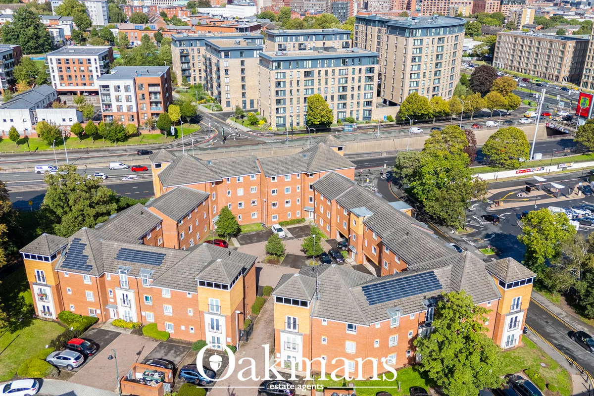 Aerial view of red-brick residential apartment complex with pitched roofs and solar panels, surrounded by contemporary m