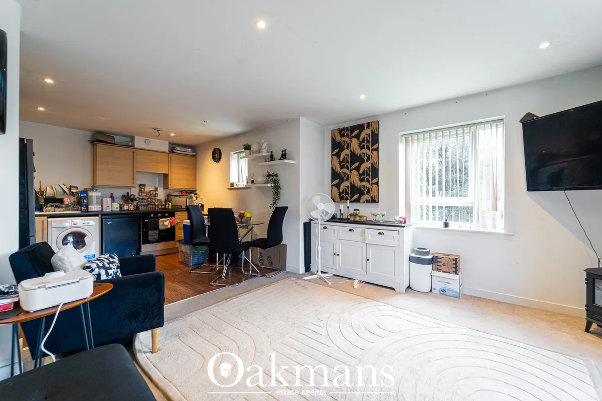 Open-plan living area with kitchen, dining space, navy armchair, white storage cabinet, wall-mounted TV, and large windo