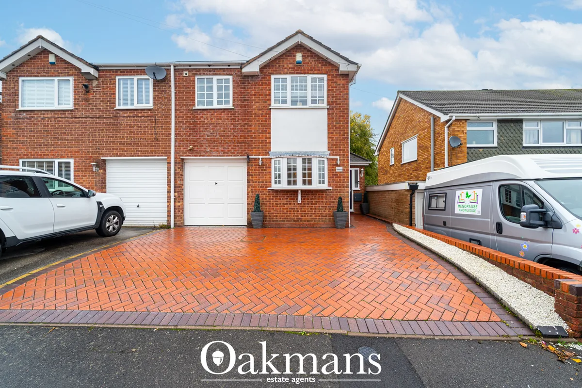 Red brick semi-detached house with double garage, driveway with herringbone brick paving, white-framed windows and parke