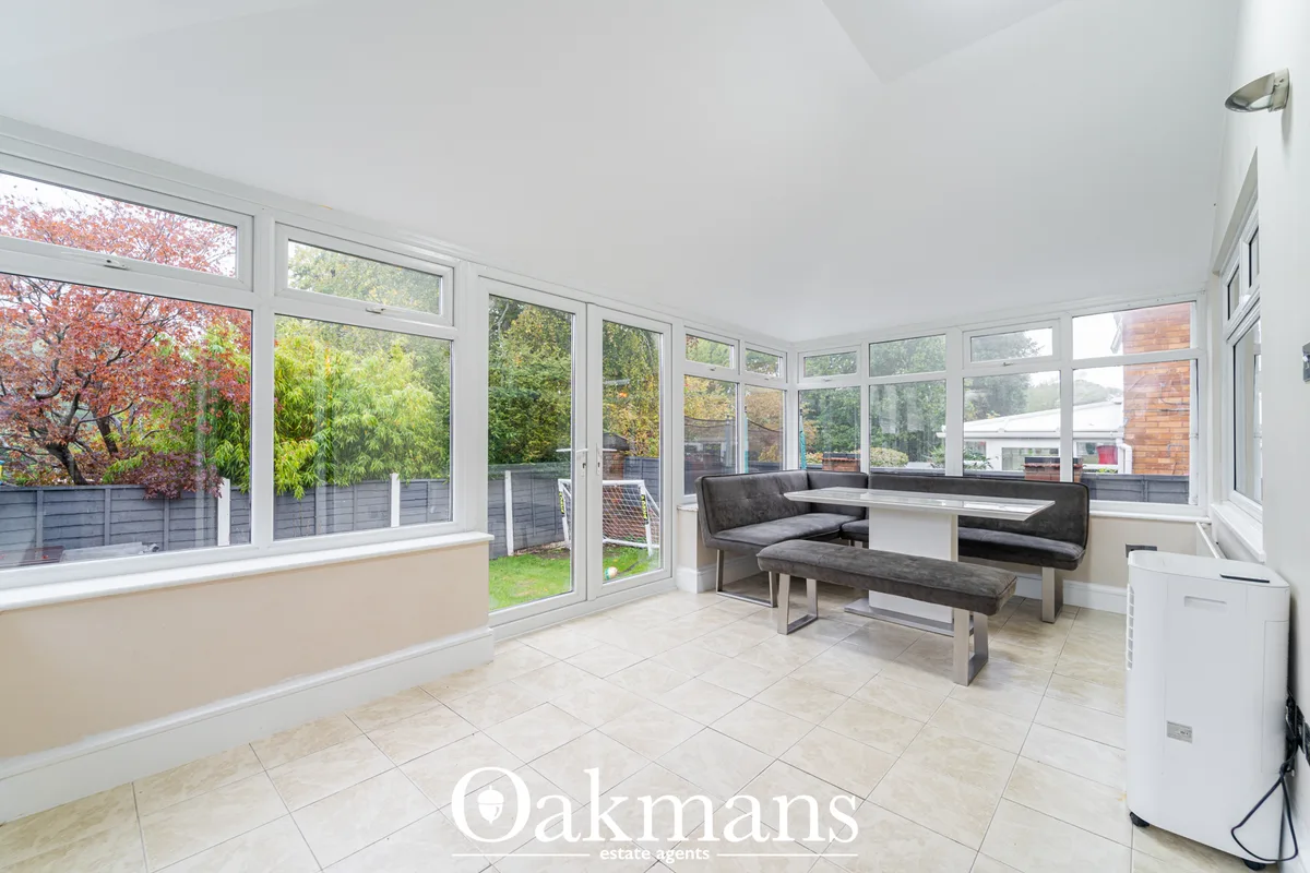 Bright conservatory with extensive glazing, grey banquette seating, dining table, tiled flooring and views over garden w